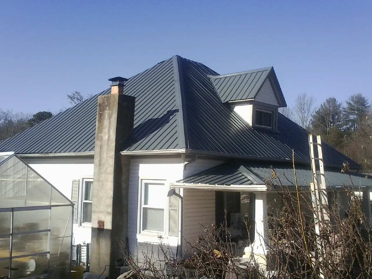 Dark blue standing seam metal roof on a white farmhouse with dormer — Slate & Tile Roof Repair by Roofing Brothers in Belle Plaine