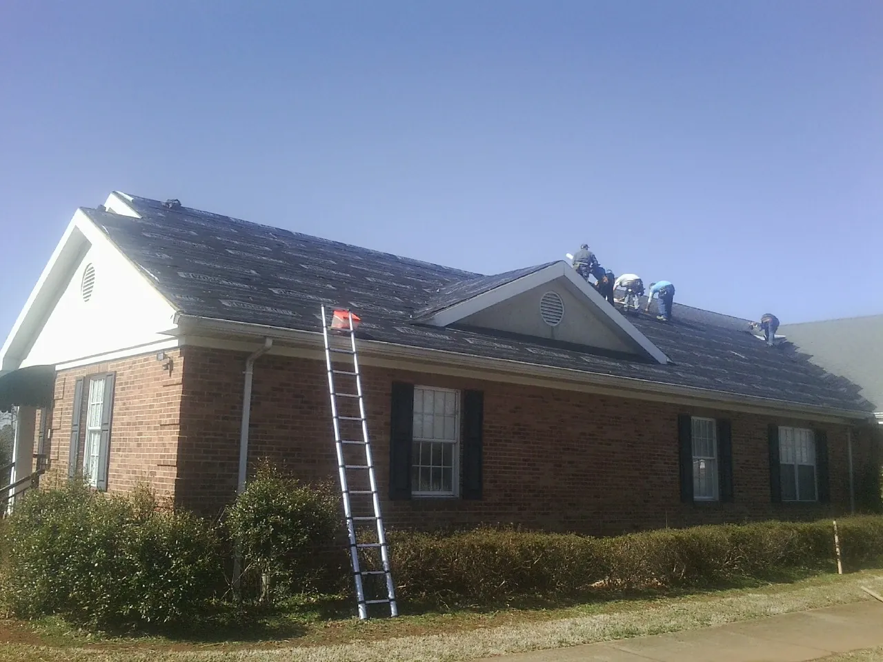 Crew tearing shingles off a brick ranch roof with a ladder set — Metal Roof Repair work by our crew in Belle Plaine