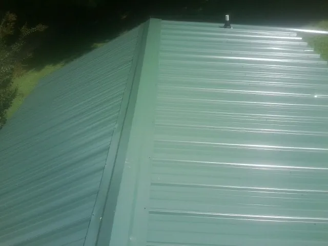 New green metal panels meeting at the ridge of a roof — Flat Roof Repair work by our crew in Belle Plaine