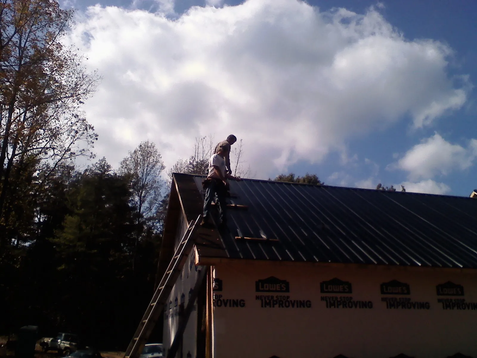Roofer fastening dark metal panels high against a cloudy sky, from a Roof Inspection job in Belle Plaine
