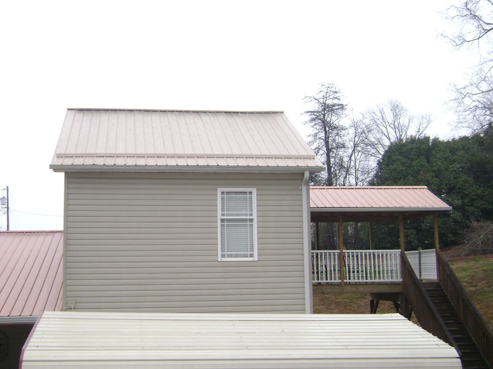 Tan metal roofs on a two story addition and attached porch, from a Roof Replacement job in Belle Plaine